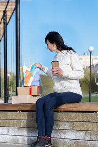 Dark-haired woman looks with interest into the gift package. outdoor portrait against the blue sky