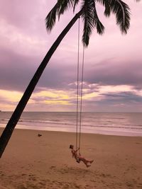 Full length woman swinging at f beach during sunset