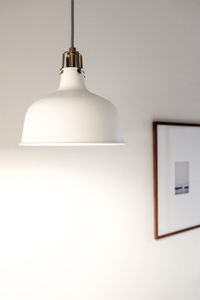 Close-up of light bulb hanging against white wall