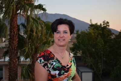 Portrait of smiling woman against trees during sunset