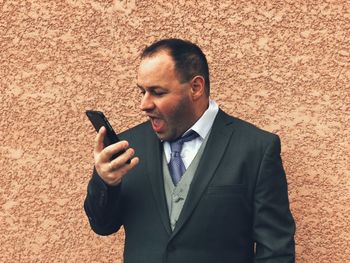 Close-up of businessman using mobile phone against wall