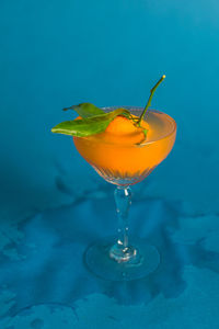 Mandarin tangerine orange fruit dropped into cocktail drink with  blue background