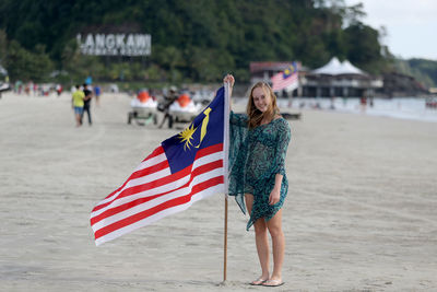 Rear view of woman holding american flag at beach