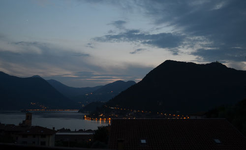 Silhouette buildings by mountains against sky during sunset