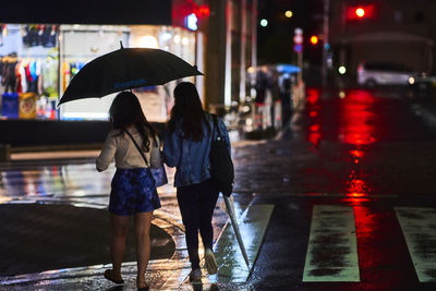 Rear view of women walking on wet street at night