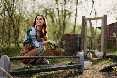 Smiling woman holding bowl of leaves in farm