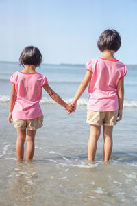 Rear view of sisters holding hands while standing on shore at beach