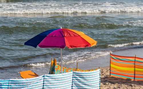 A colorful umbrella spread out on the beach on a beautiful sunny summer day with a rough sea.