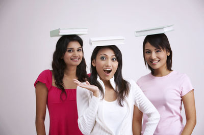 Portrait of smiling friends with books on heads against white background