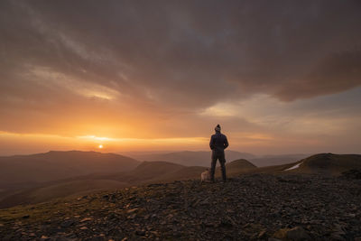 Rear view of man standing on mountain against sunset sky