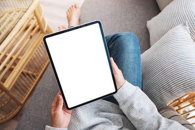 Midsection of woman using digital tablet while sitting on sofa at home