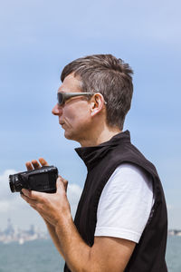 Side view of man photographing against sky