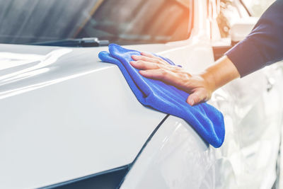 Cropped hand of man cleaning car with blue towel