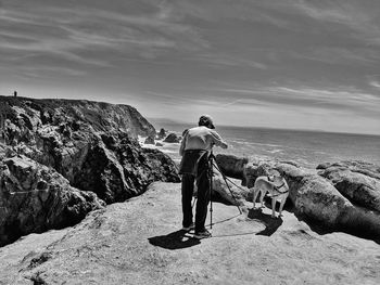 Rear view of man on rock at beach against sky