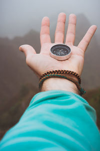 Cropped hand of man holding navigational compass against mountains