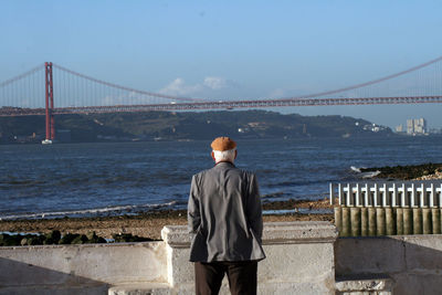 Rear view of man standing against suspension bridge over sea