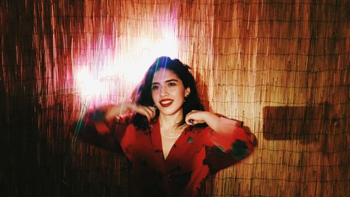 Portrait of beautiful young woman standing against curtain