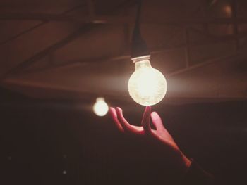 Cropped hand holding illuminated light bulb in darkroom