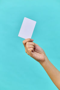 Cropped hand of woman holding paper against blue background