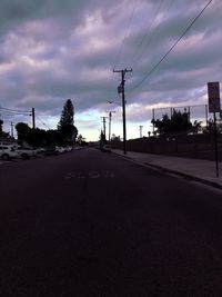 Road by electricity pylon against sky during sunset