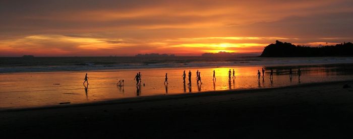 Silhouette people at beach against sky during sunset