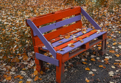 High angle view of empty bench by fallen autumn leaves at park