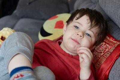 Expressive young boy eating an apple and lounging on the couch at home