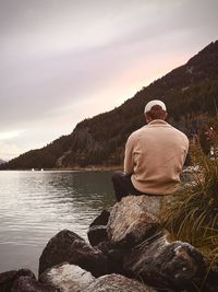 Rear view of man sitting on rock against sky