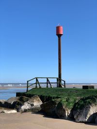 Lighthouse by sea against clear blue sky