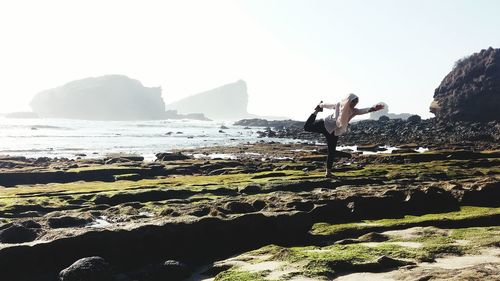 Man standing on cliff by sea against clear sky