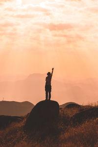 Silhouette man standing on rock against sky during sunset