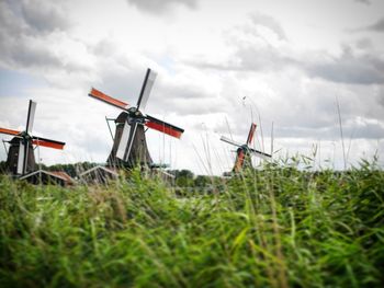 Low angle view of traditional windmills on grassy field against cloudy sky