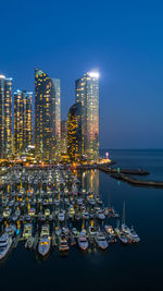 Illuminated modern buildings by sea against sky at night