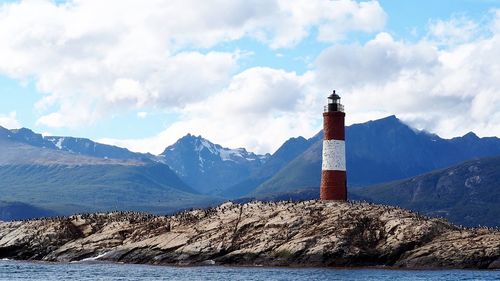 Lighthouse amidst buildings and mountains against sky