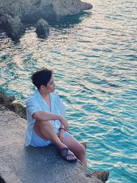 Side view of woman sitting on rock by lake