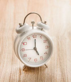 Close-up of white alarm clock on wooden table