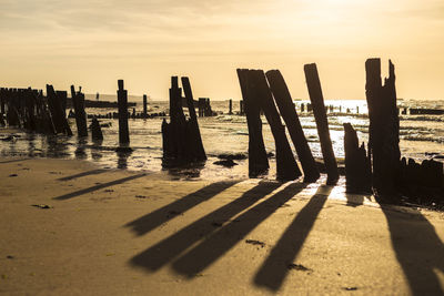 Wooden posts on beach against sky during sunset