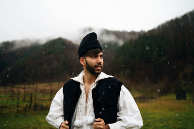 Man wearing warm clothing looking away while standing on land