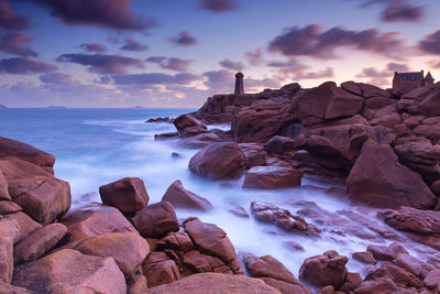 Rocks in sea against sky during sunset