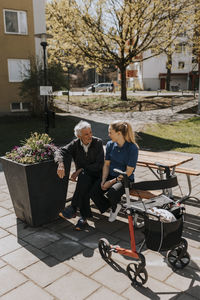 Senior man talking to female care assistant while sitting on bench