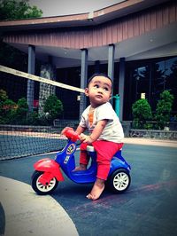 Full length of cute boy sitting on toy car outdoors