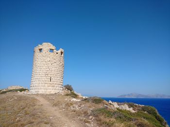 Old ruin on hill by sea against clear blue sky