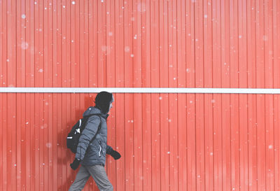 Side view of mid adult man with umbrella walking against wall during snowfall