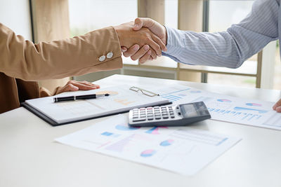 Midsection of businessman and businesswoman shaking hands over table in office