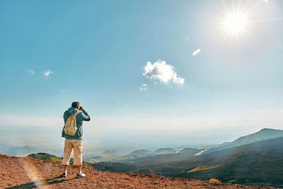 Rear view of man looking through binoculars at panoramic view of summits volcano etna