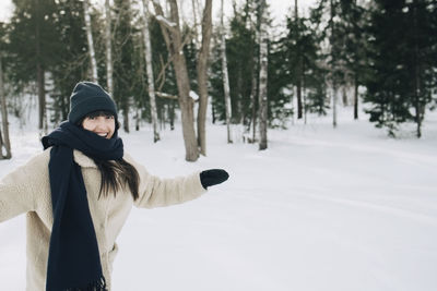 Portrait of happy woman standing with arms outstretched on snow covered landscape