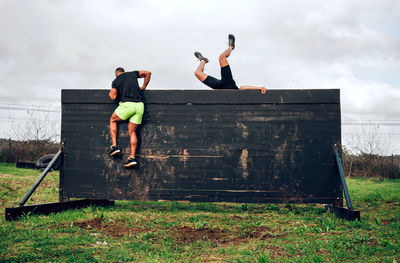 Men climbing wooden wall against cloudy sky