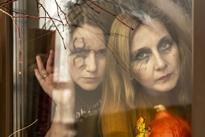 Two female witches look through a spider web ominously out of the window .halloween party.
