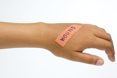 Cropped hand of woman with wound text on bandage against white background