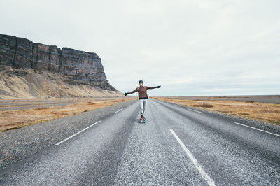 Man skateboarding on road against sky